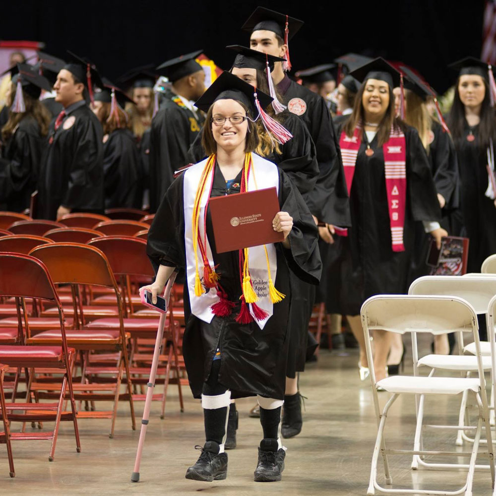 graduating student with Leg braces and a cane walking with her diploma during a graduation ceremony
